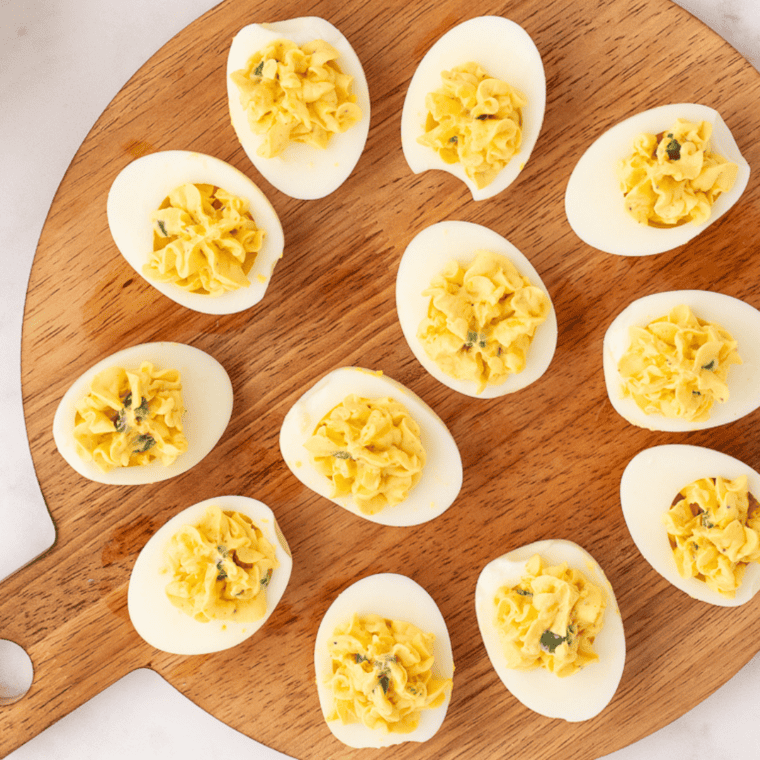 Finished million dollar deviled eggs on a platter, piped and topped with bacon and paprika