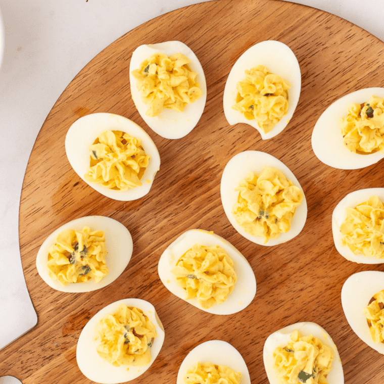 Plate of million dollar deviled eggs piped with a star tip and topped with paprika and crumbled bacon
