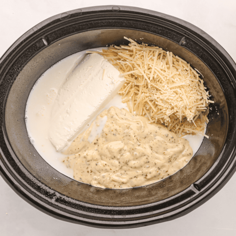 Seasoned raw chicken breasts arranged in a single layer in a slow cooker.