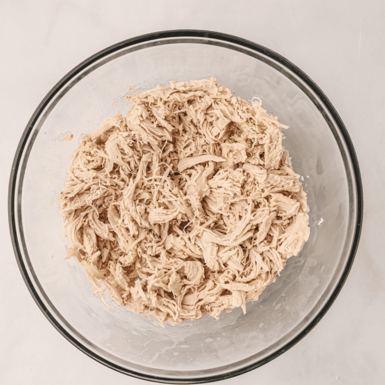 Juicy slow cooker shredded chicken piled in a white serving bowl