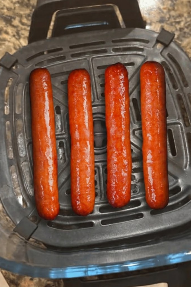 Frozen hot dogs cooking in an air fryer basket until hot, juicy, and lightly crisp on the outside, ready to serve in buns.