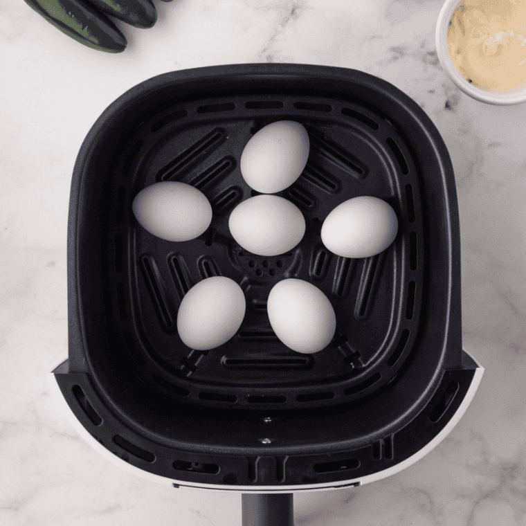 Hard boiled eggs cooking in an air fryer basket for jalapeño deviled eggs