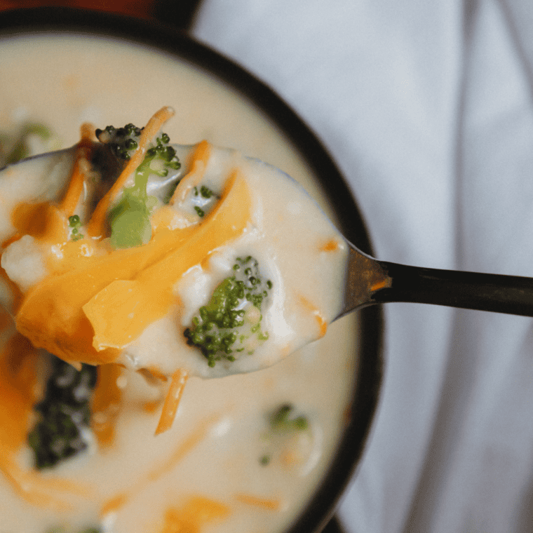 A bowl of creamy broccoli cheddar soup made in the Ninja Foodi, garnished with shredded cheddar and broccoli florets.