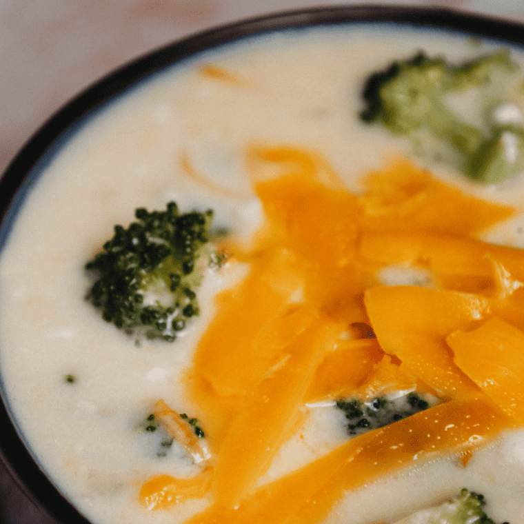 A bowl of creamy broccoli cheddar soup made in the Ninja Foodi, garnished with shredded cheddar and broccoli florets.