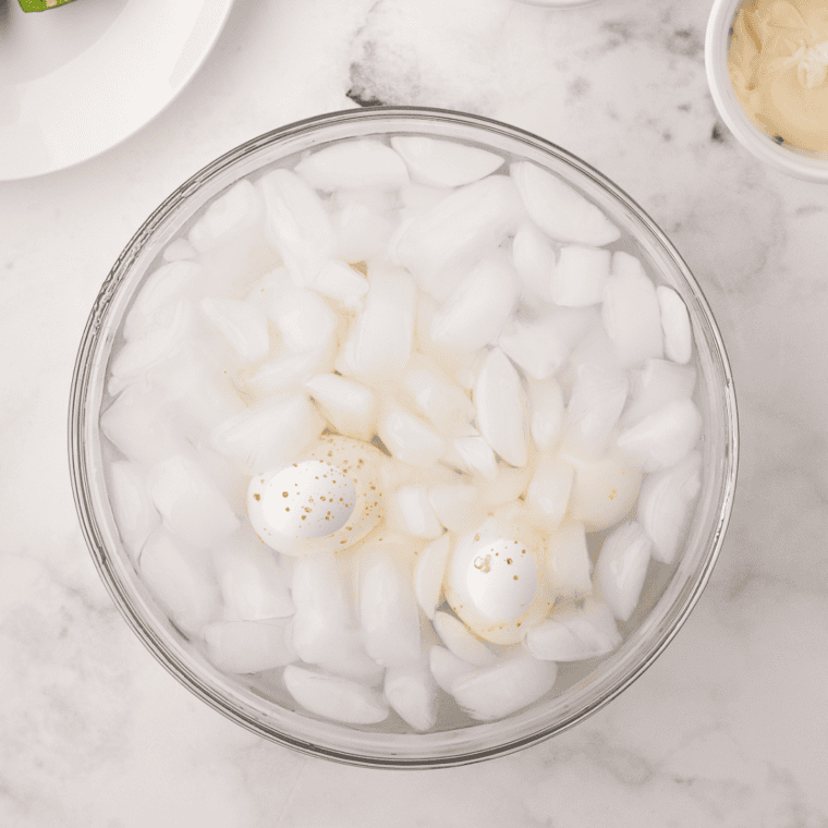 Using tongs to transfer Ninja Foodi hard-boiled eggs into an ice water bath to stop cooking and make peeling easier.