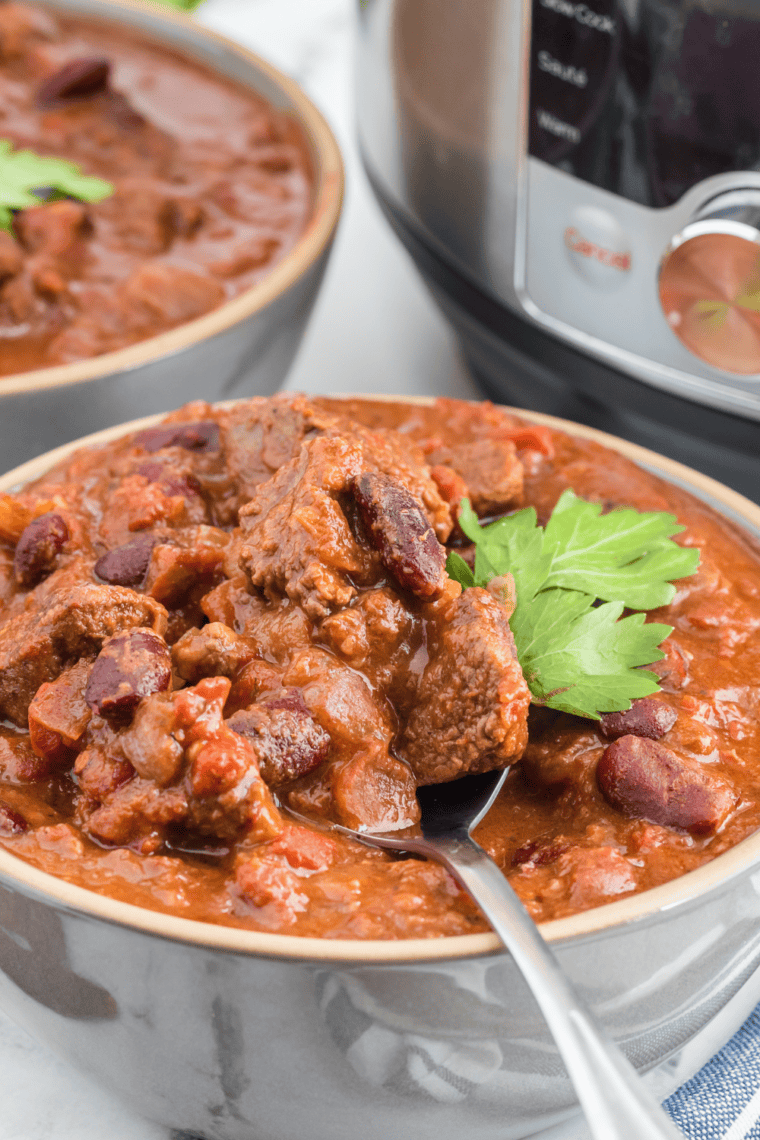 A hearty bowl of Air Fryer Chili Con Carne, showcasing a rich blend of ground beef, kidney beans, and tomatoes, garnished with fresh cilantro and served with a side of crunchy tortilla chips.