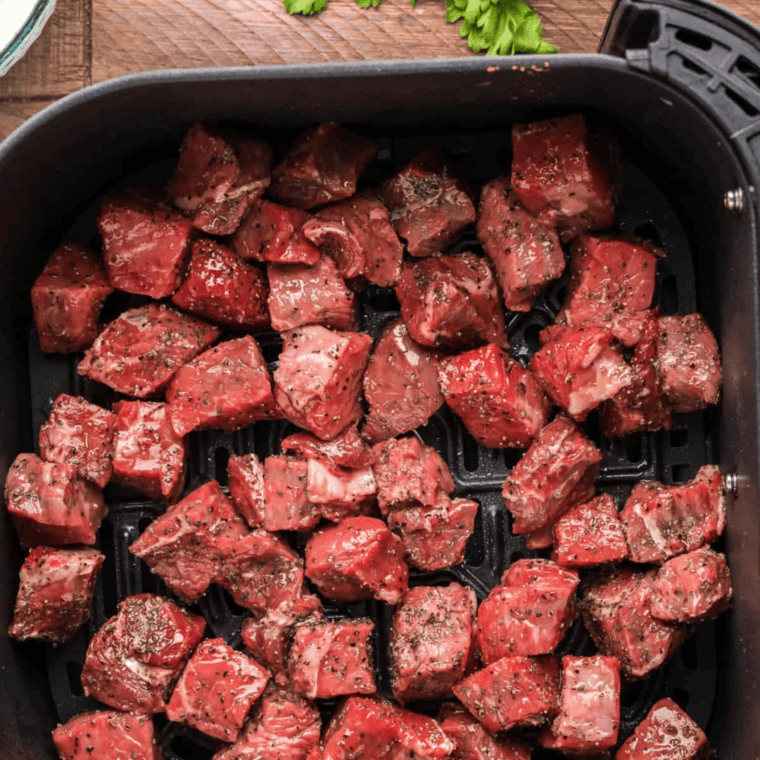 Cooking beef - A photo beef browning in the air fryer basket, with spices sprinkled on top, showcasing the cooking process.