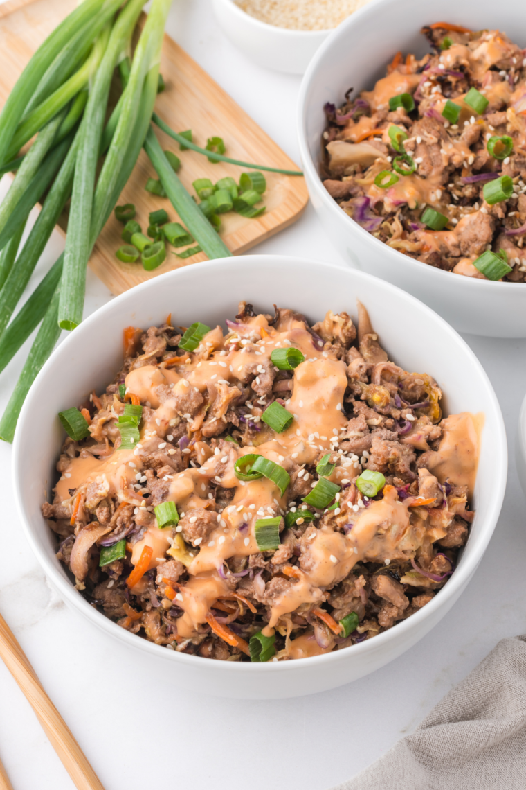 A hearty serving of Air Fryer Egg Roll In A Bowl, showcasing a vibrant mix of sautéed cabbage, carrots, and ground meat, garnished with chopped green onions and sesame seeds, presented in a bowl with chopsticks on the side.