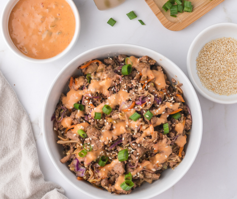 A colorful bowl of Air Fryer Egg Roll In A Bowl, featuring shredded cabbage, carrots, and protein, garnished with green onions and sesame seeds, served with soy sauce on the side.