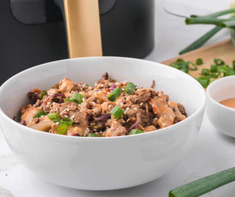  
A vibrant serving of Air Fryer Egg Roll In A Bowl, showcasing a mix of sautéed cabbage, carrots, and ground meat, topped with chopped green onions and sesame seeds, with a pair of chopsticks resting on the side.