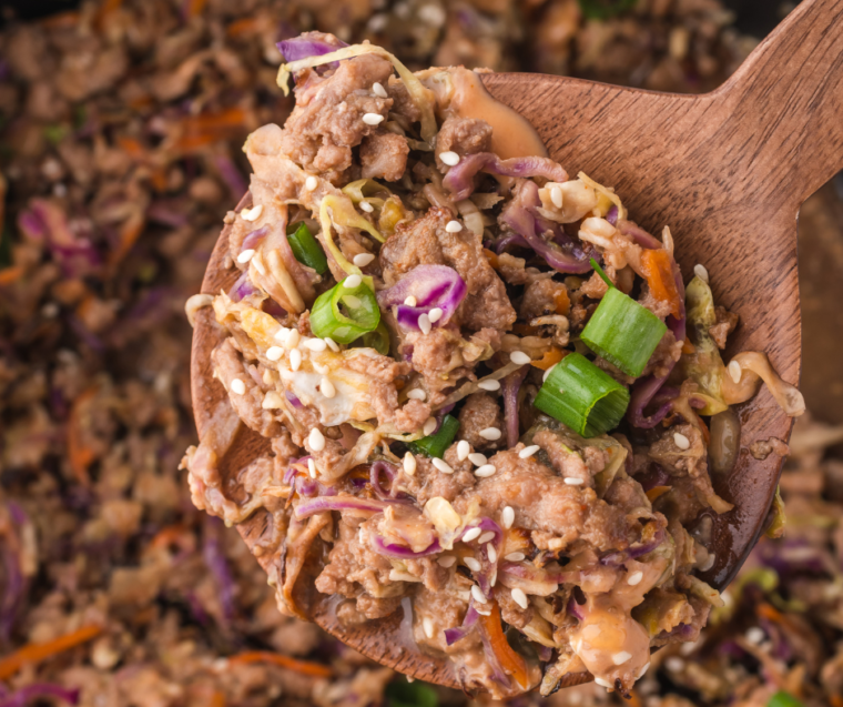A delicious bowl of Air Fryer Egg Roll In A Bowl, filled with colorful stir-fried vegetables, ground meat, and topped with sliced green onions and sesame seeds, served with a small dish of soy sauce nearby.