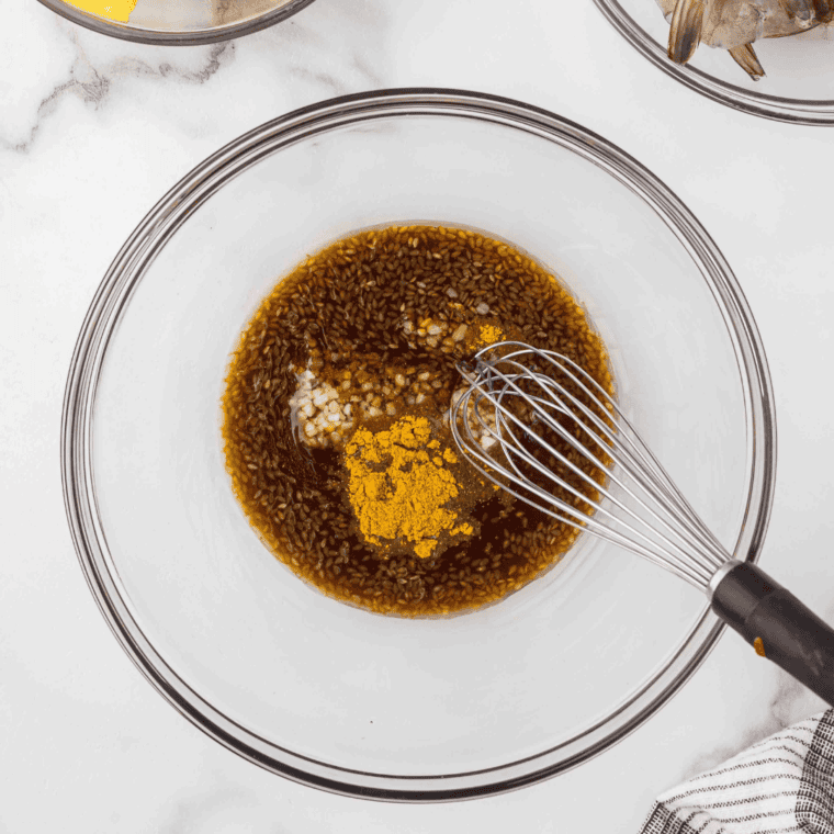 Teriyaki marinade with garlic, olive oil, and curry powder mixed in bowl with wooden skewers soaking in water.
