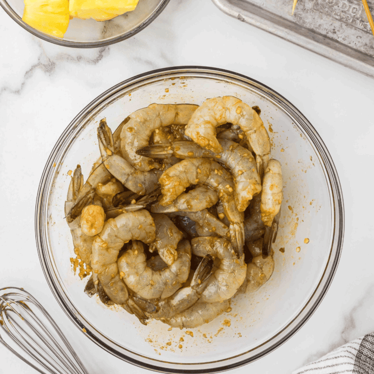 Raw shrimp marinating in Hawaiian-style teriyaki sauce in a mixing bowl.
