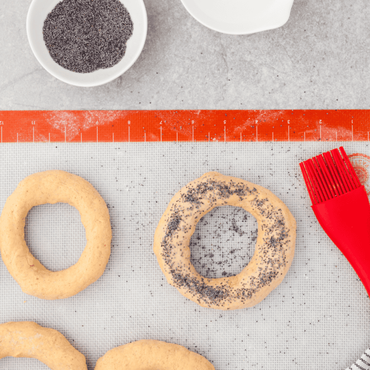 Pumpkin Bagels being dusted with poppy seeds