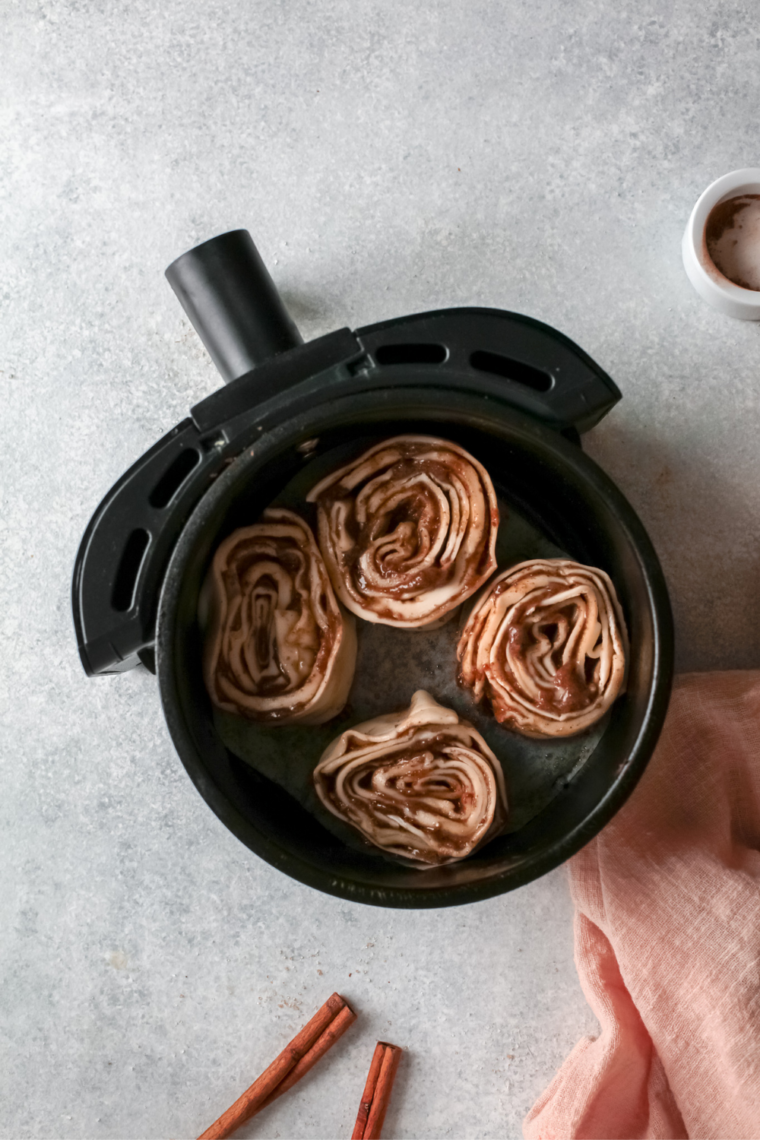 Cinnamon rolls arranged on parchment paper in air fryer basket, cooking at 300°F then 350°F.