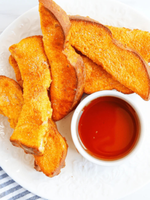 Air fryer pumpkin French toast sticks stacked on a plate with a bowl of maple syrup for dipping