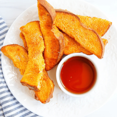 Air fryer pumpkin French toast sticks stacked on a plate with a bowl of maple syrup for dipping