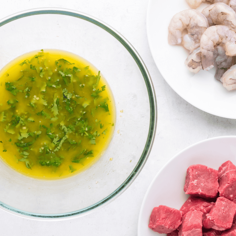 Ingredients for Air Fryer Surf and Turf: raw steak, shrimp, olive oil, garlic, butter, salt, pepper, and fresh herbs on a wooden cutting board.