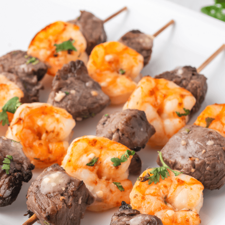Perfectly seared steak and golden shrimp cooked in the air fryer, garnished with fresh herbs and served on a white plate.