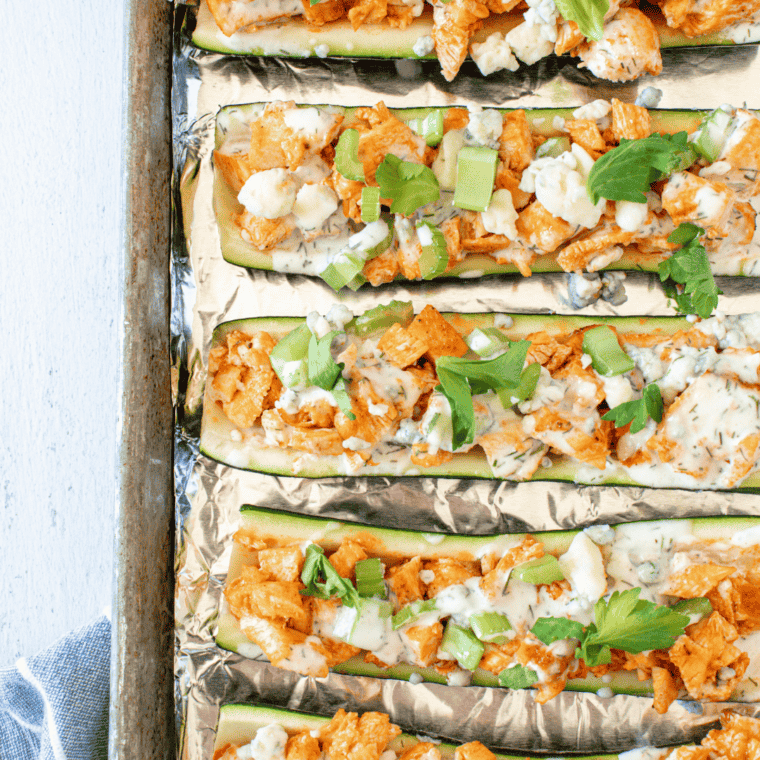 Filling zucchini halves with the Buffalo chicken mixture using a spoon.