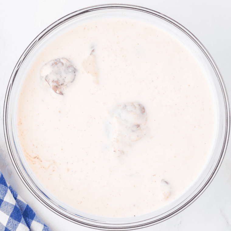 Marinating chicken pieces in a bowl of buttermilk, demonstrating the first step in preparing Air Fryer Southern Fried Chicken.