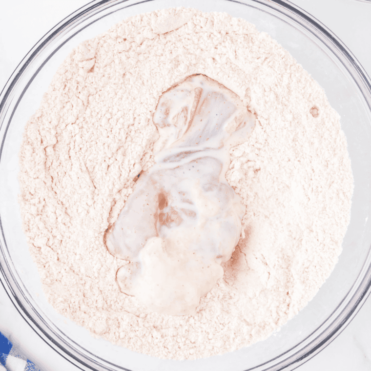 Coating marinated chicken in seasoned flour, with hands covered in flour for a rustic cooking process.