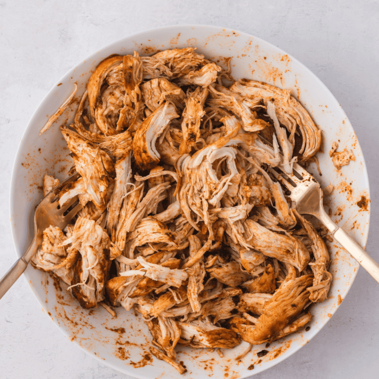 Shredding cooked chicken breasts with two forks on a cutting board.