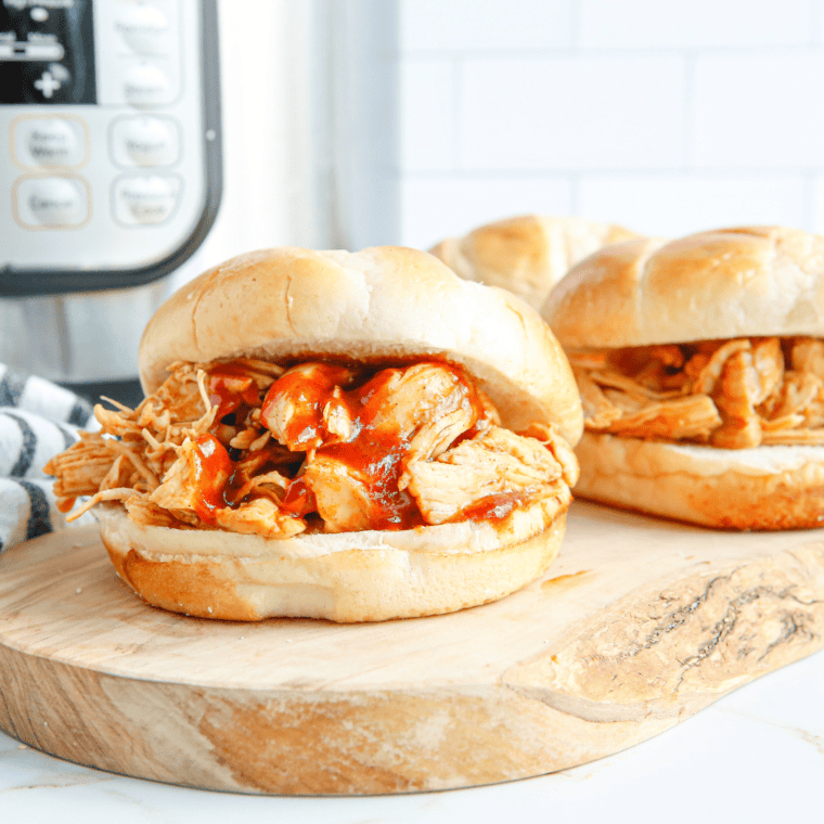 Instant Pot BBQ shredded chicken coated in glossy barbecue sauce inside the pressure cooker.