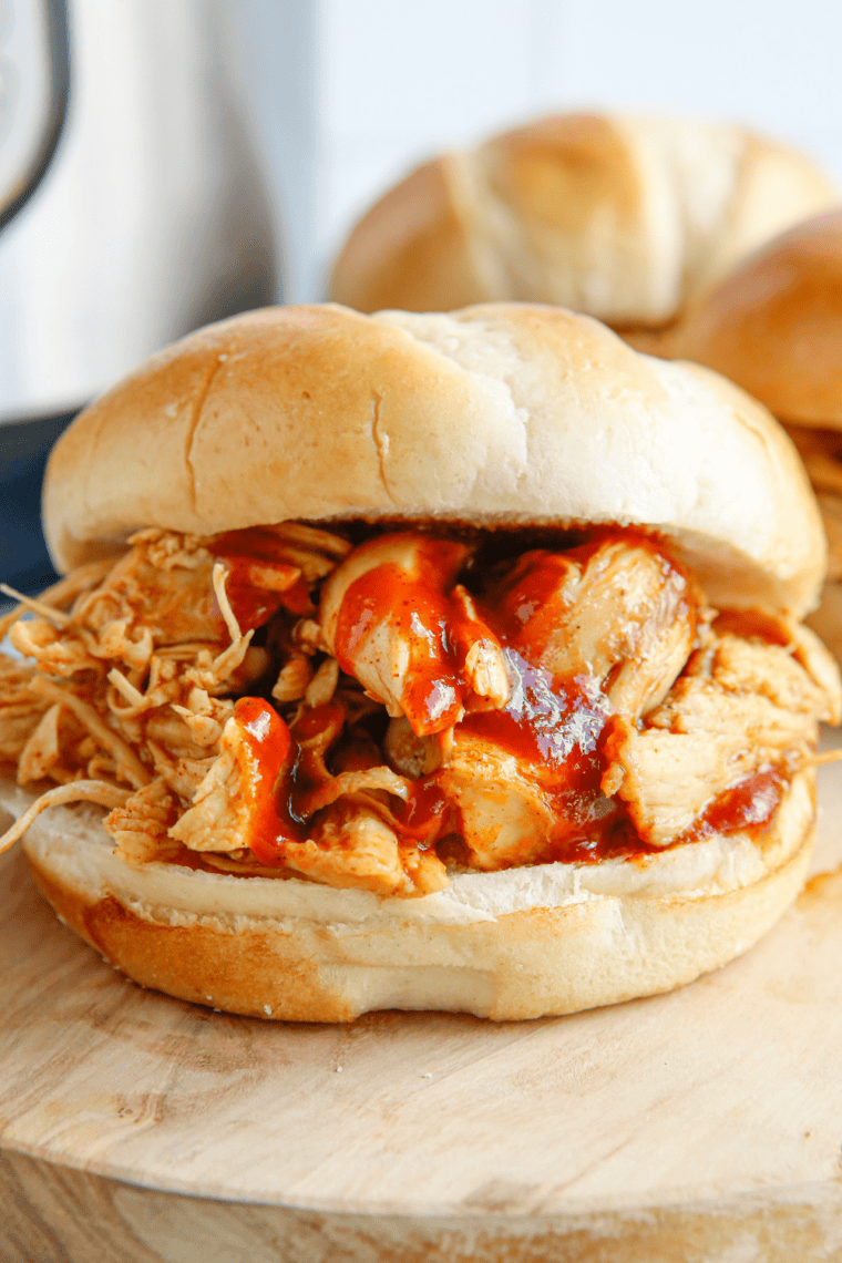Instant Pot BBQ shredded chicken piled on a toasted bun with the Instant Pot in the background.