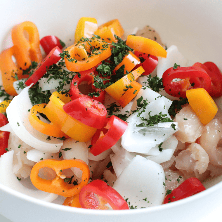 Sliced chicken and bell peppers tossed with fajita seasoning and lime juice in a glass mixing bowl