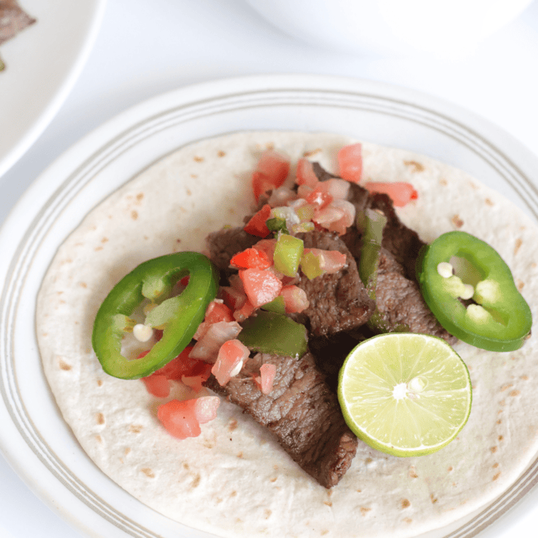 Grilled steak fajitas with onions and bell peppers served on a plate.