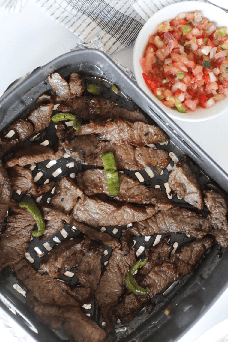 Marinated flank steak slices cooking on a preheated Ninja Foodi Grill with visible grill marks.