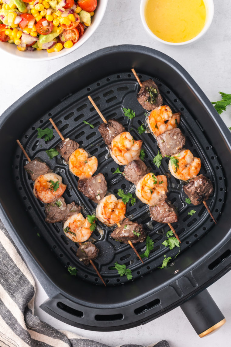 "Freshly cooked surf and turf kebabs brushed with melted butter, garnished with fresh herbs, and resting before serving."