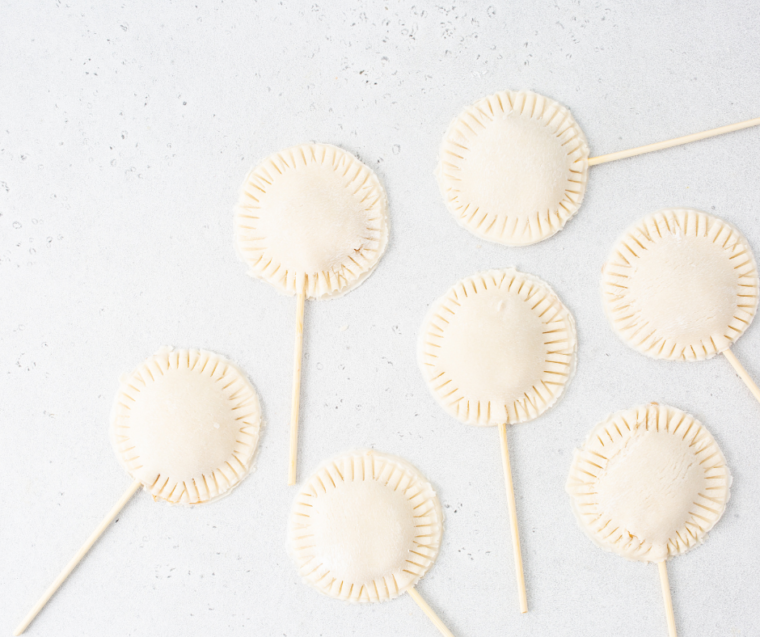 Pie dough cutouts on baking sheet with lollipop sticks inserted and apple filling spooned in the center