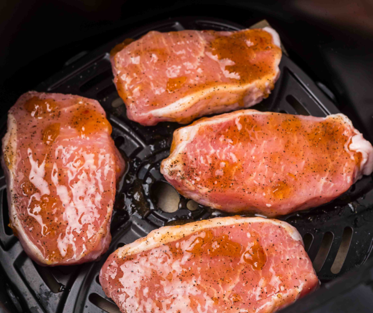 Marinated pork chops arranged in a single layer in the air fryer basket