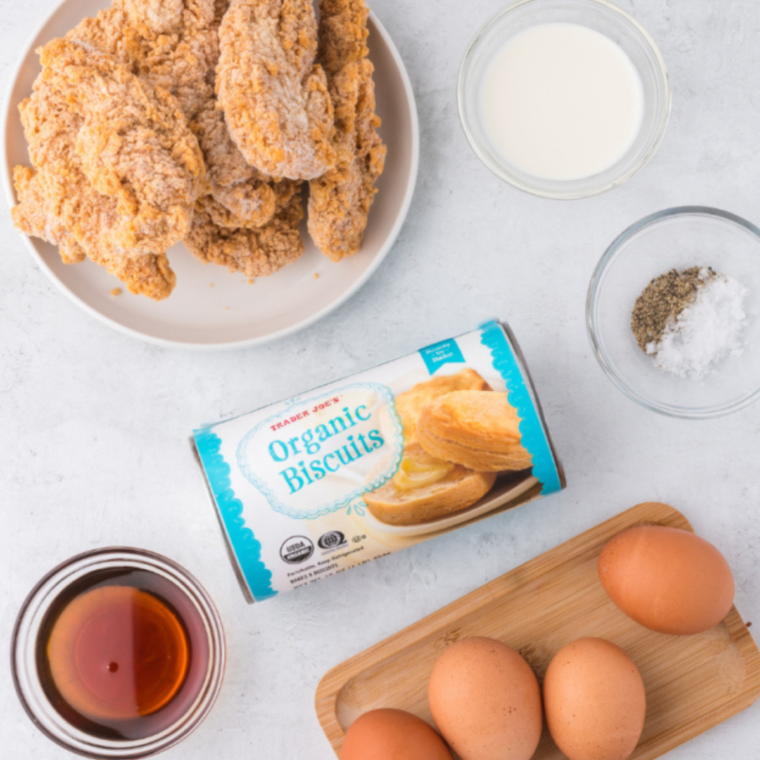 Ingredients for Air Fryer Chicken Biscuit Sandwiches: canned biscuits, breaded chicken, and maple syrup on a marble counter