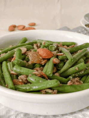 Crisp green beans topped with golden toasted almonds and garlic, cooked in the air fryer and served in a white dish.