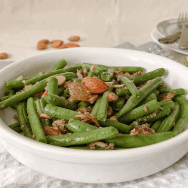 Crisp green beans topped with golden toasted almonds and garlic, cooked in the air fryer and served in a white dish.