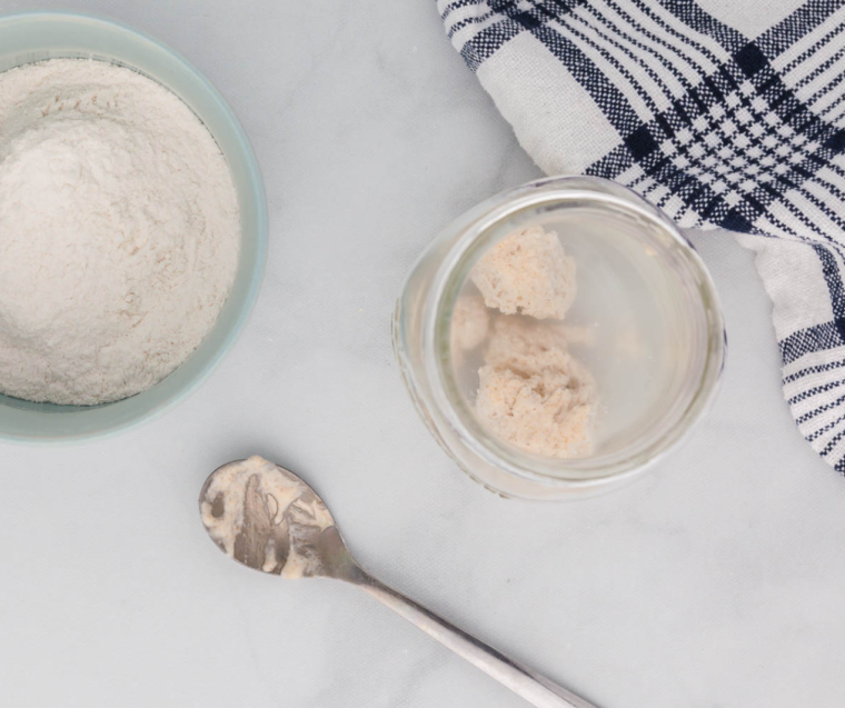 Mixing sourdough starter with lukewarm water and flour in a glass jar for air fryer bread