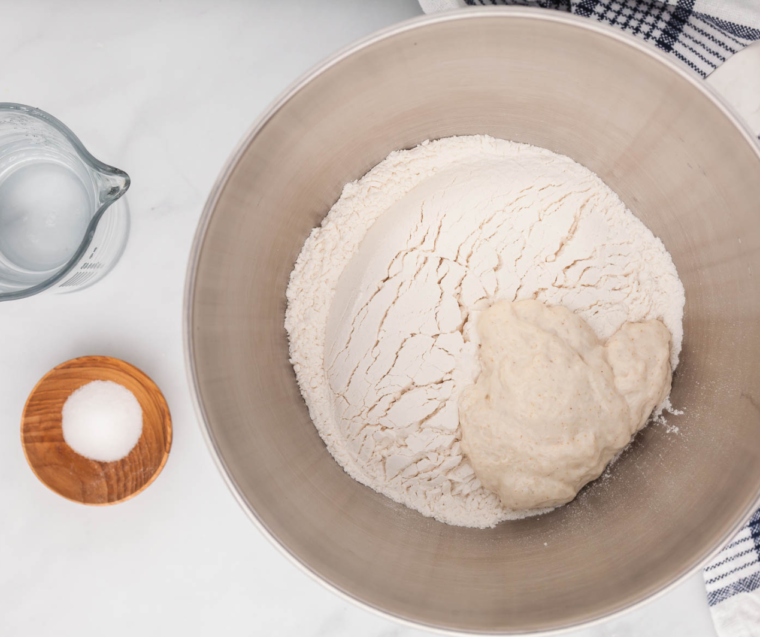 Mixing sourdough bread dough ingredients in a large bowl with flour, salt, and starter