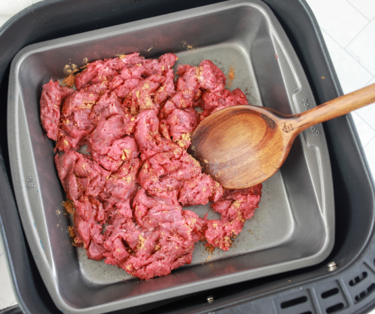 Raw ground beef tossed with taco seasoning in a glass mixing bowl