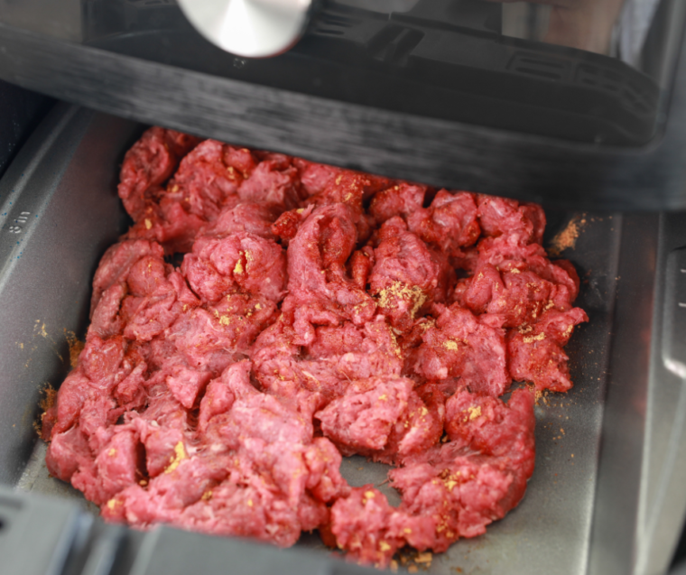 Seasoned beef pressed into an even layer in the air fryer basket before cooking