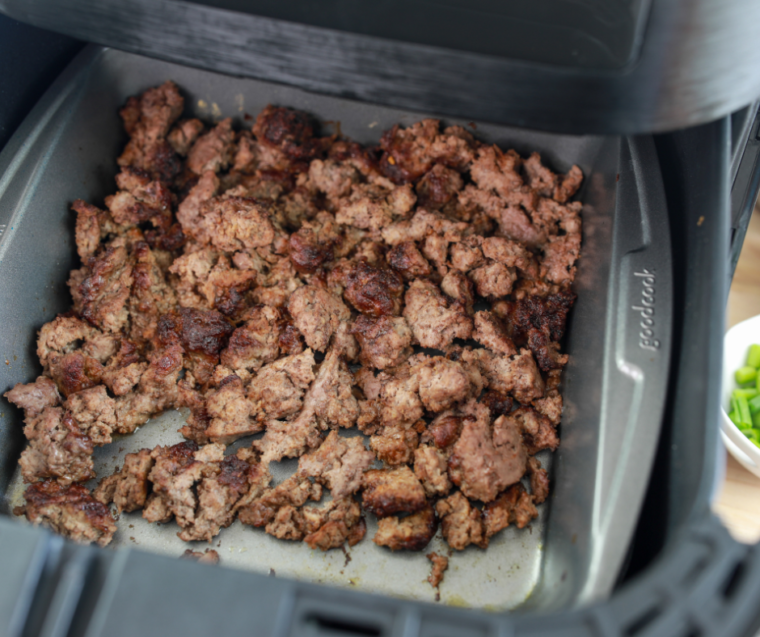 Browned taco meat broken into crumbles with a wooden spoon in the air fryer