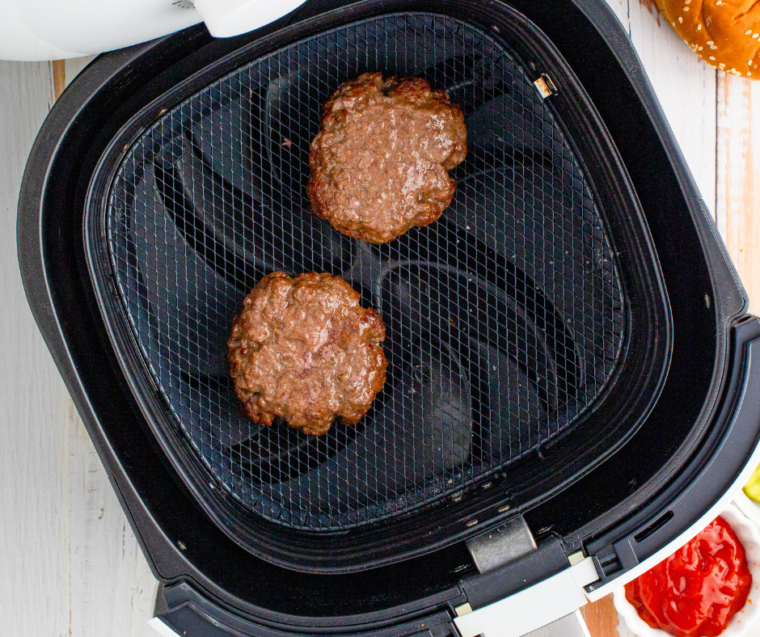 Beef patties placed in an air fryer basket, cooking.