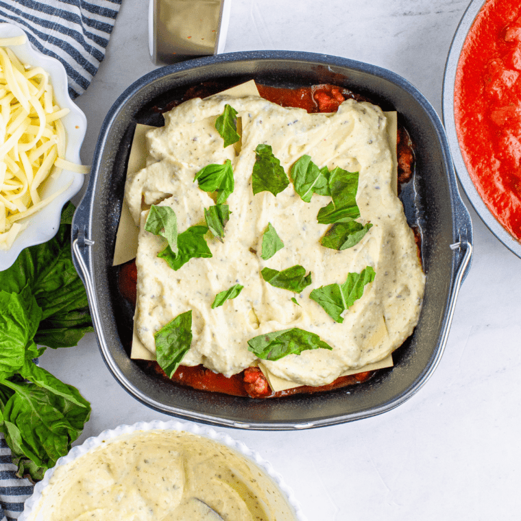 Spreading ricotta cheese filling and fresh basil leaves over lasagna noodles in air fryer baking dish