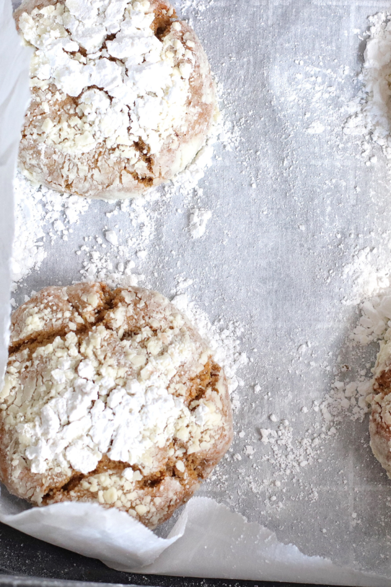 Freshly baked gingerbread crinkle cookies with a signature cracked powdered sugar surface and soft, dark molasses centers arranged on a cooling rack.