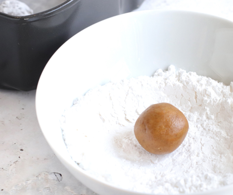 Cookie dough balls being rolled first in granulated sugar then in powdered sugar before air fryer baking.
