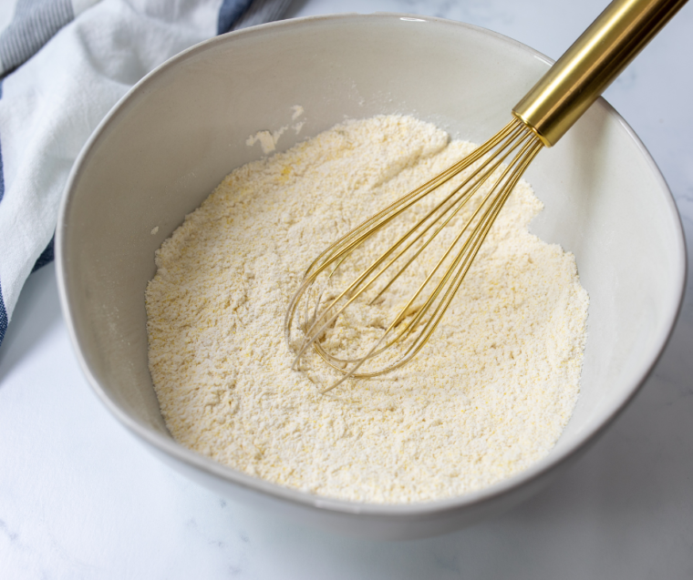 Folding charred corn, cotija cheese and cilantro into corn fritter batter in a bowl