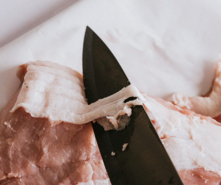 Trimmed pork tenderloin being patted dry with paper towels before seasoning