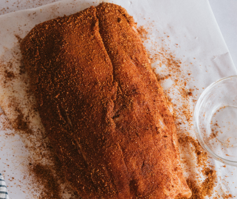 Pork tenderloin coated with olive oil and seasoned with a spice mixture in a small bowl